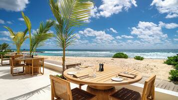 Ein Esszimmer mit Holztisch und Stühlen, mit Blick auf einen Strand mit Palmen und dem Meer.