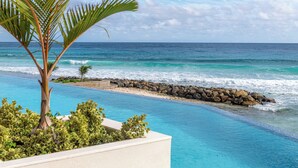 A pool with clear blue water, a palm tree, and a view of the ocean. - Hotel Indigo Bridgetown Barbados by IHG (Hastings)