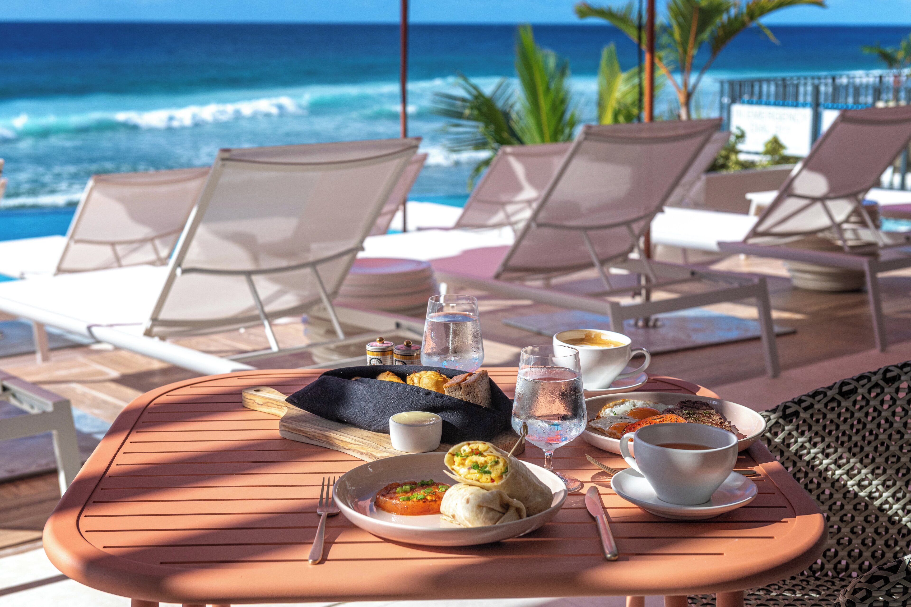 Ein Tisch mit einer Mahlzeit, einem Glas Wasser und einer Tasse Kaffee auf einer sonnigen Terrasse mit Blick auf das Meer.