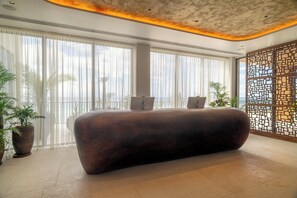 A modern lobby with a large reception desk, large windows with sheer curtains, and a decorative wall panel. - Hotel Indigo Bridgetown Barbados by IHG (Hastings)