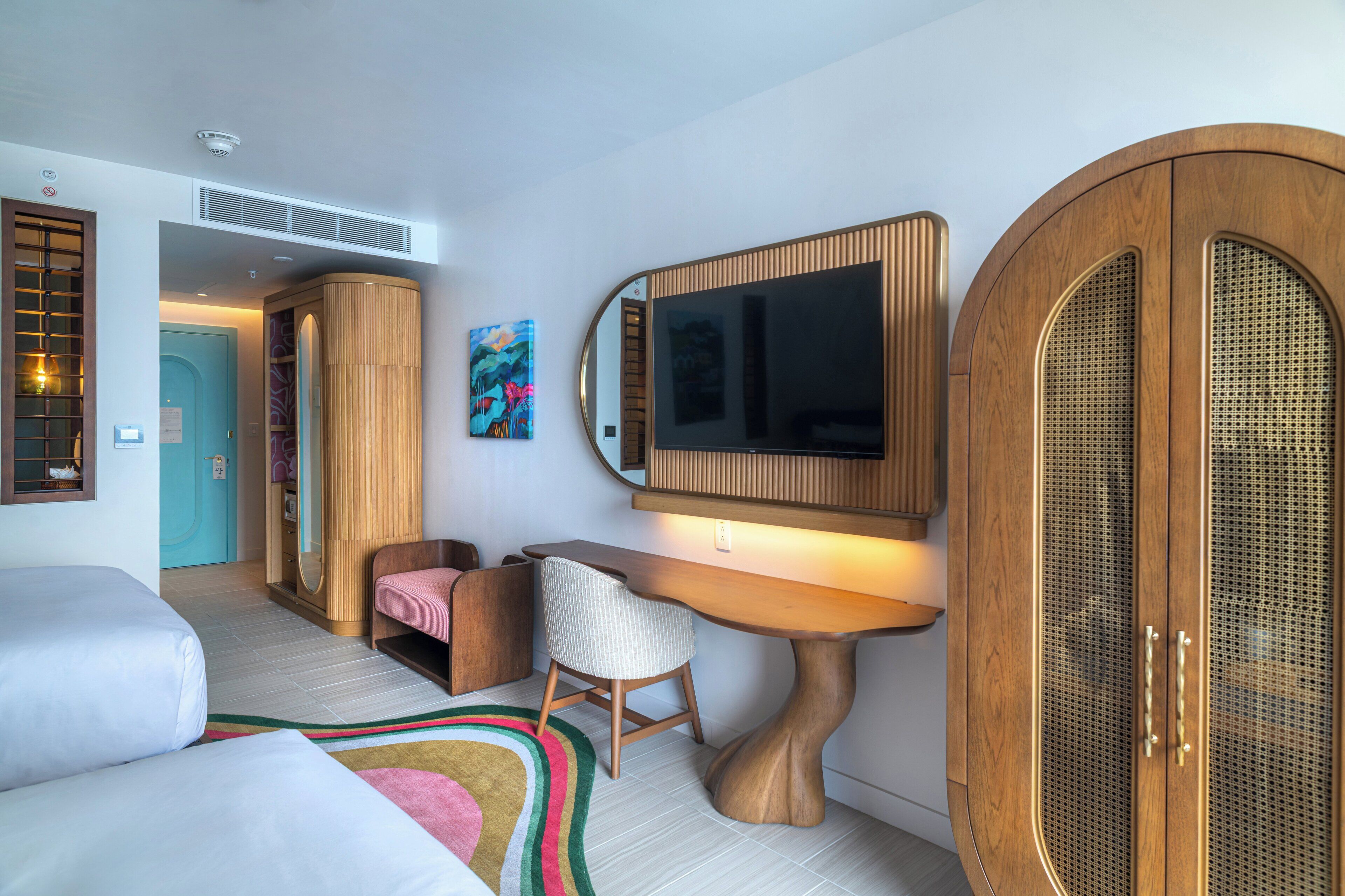 Une chambre d’hôtel moderne avec un bureau en bois, un grand miroir, une télévision et une armoire.