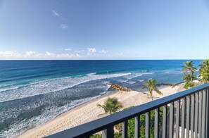A beach view from a balcony with a railing, ocean waves, and palm trees. - Hotel Indigo Bridgetown Barbados by IHG (Hastings)