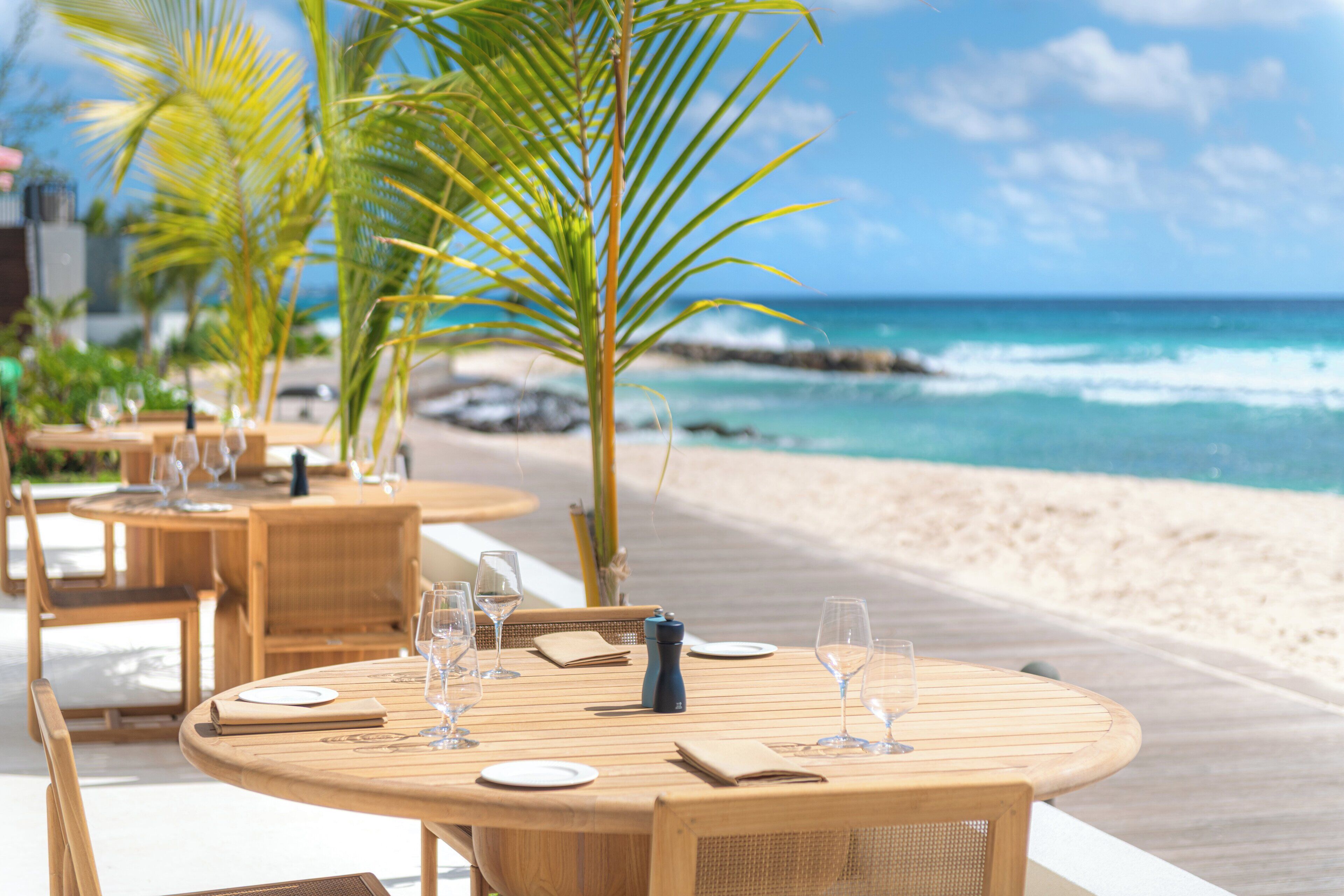Un restaurant situé en bord de mer, avec des tables et des chaises en bois rondes, et une vue sur l’océan.