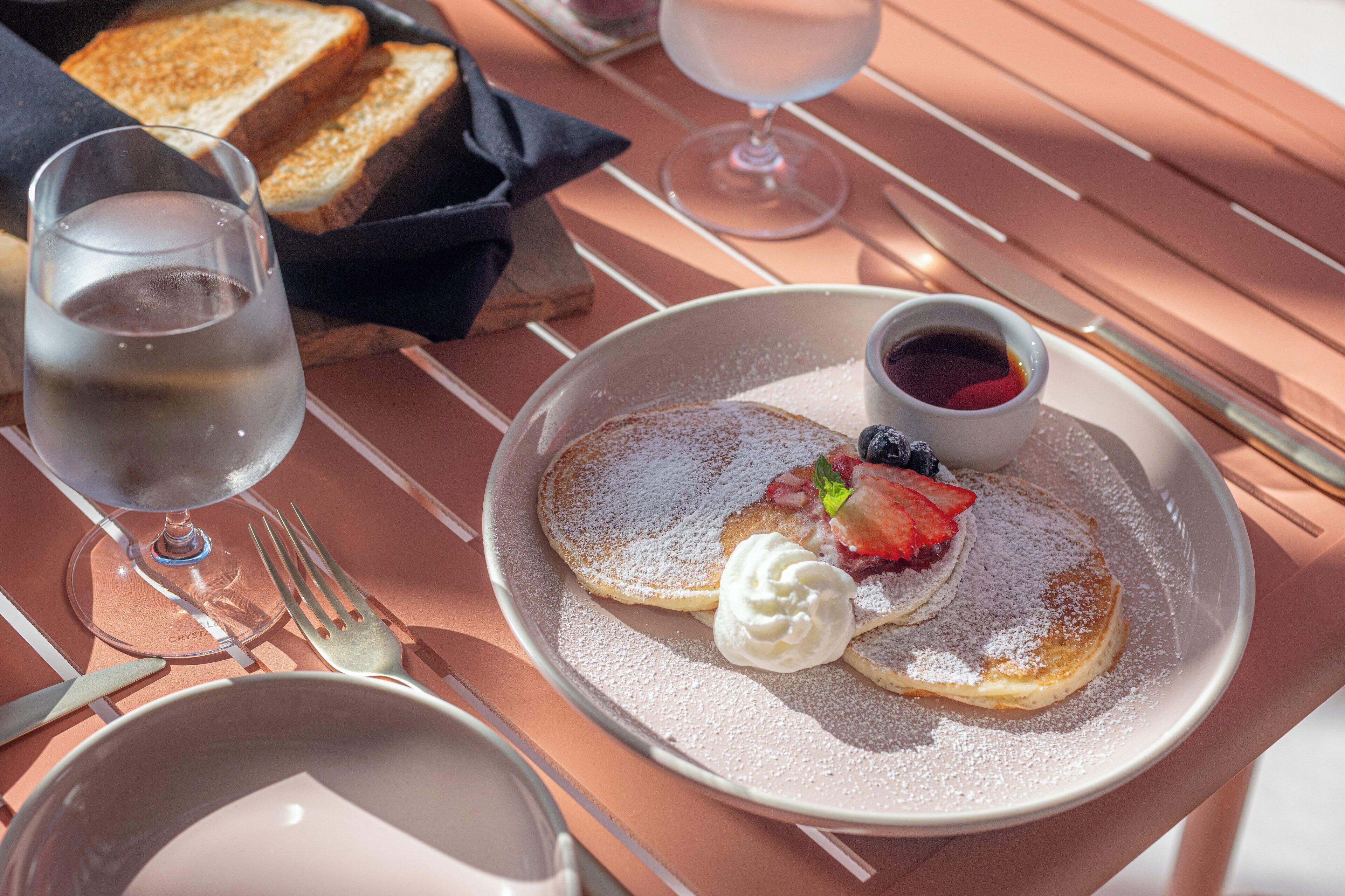 A breakfast setting with toast, whipped cream, and berries on a plate, accompanied by a glass of wine and a cup of coffee.
