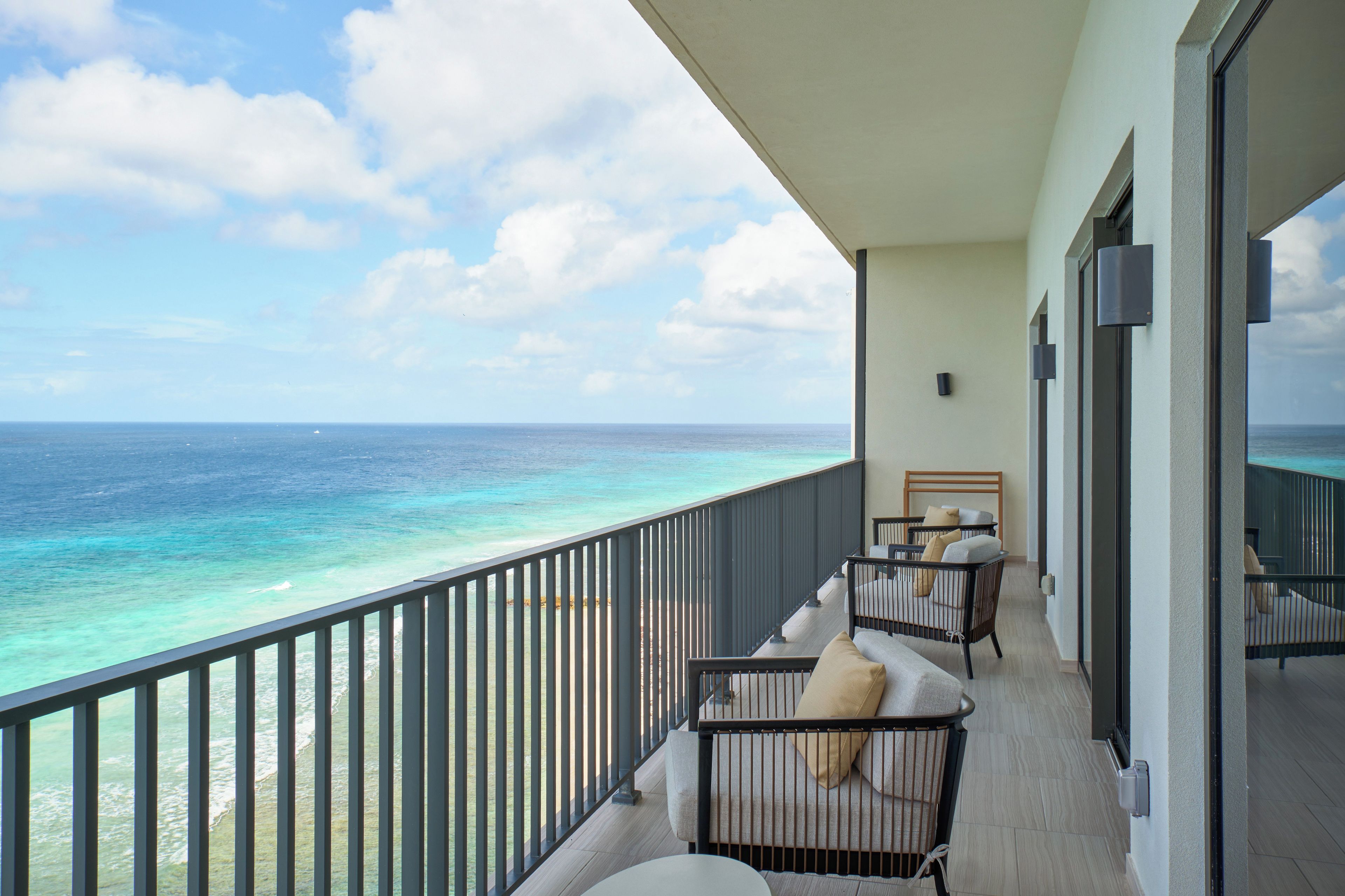 A balcony with a view of the ocean, a railing, and a seating area with cushions.