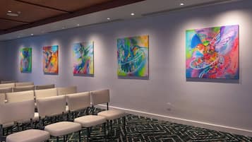 Un vestíbulo de hotel con una hilera de sillas color beige, una alfombra estampada y pinturas abstractas coloridas en las paredes.