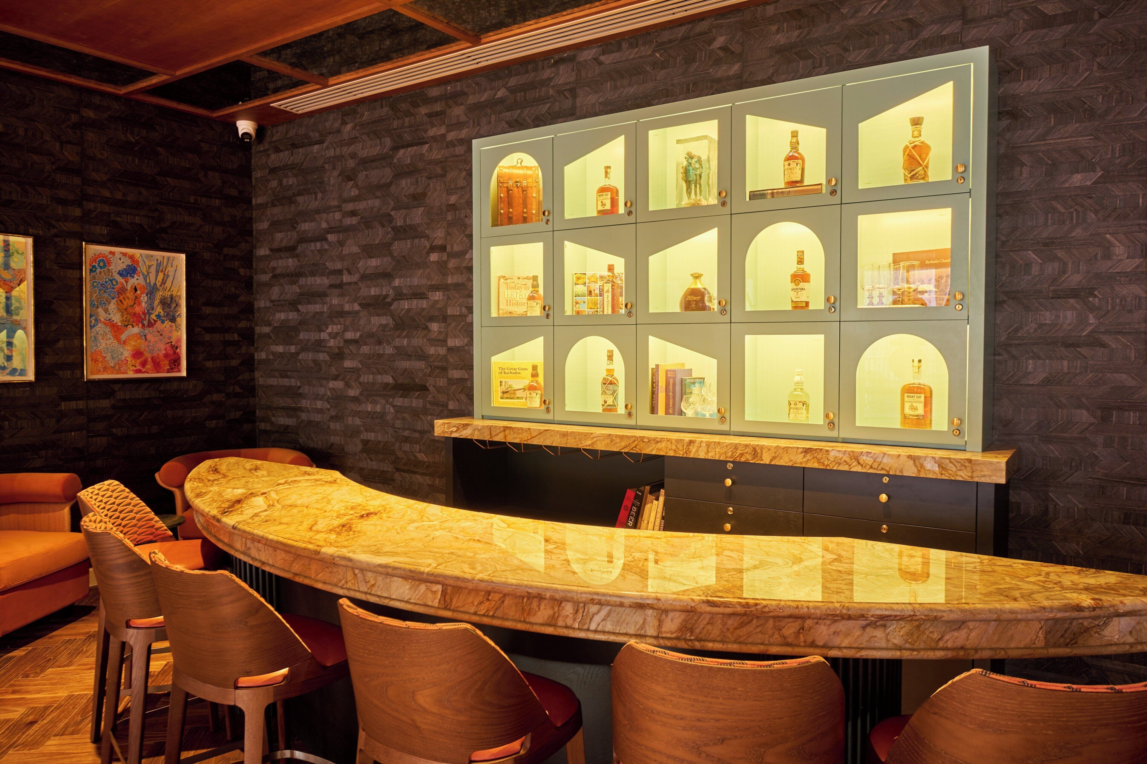 Zona de bar con una barra de mármol curvada, varios taburetes y una exhibición de botellas de licor.