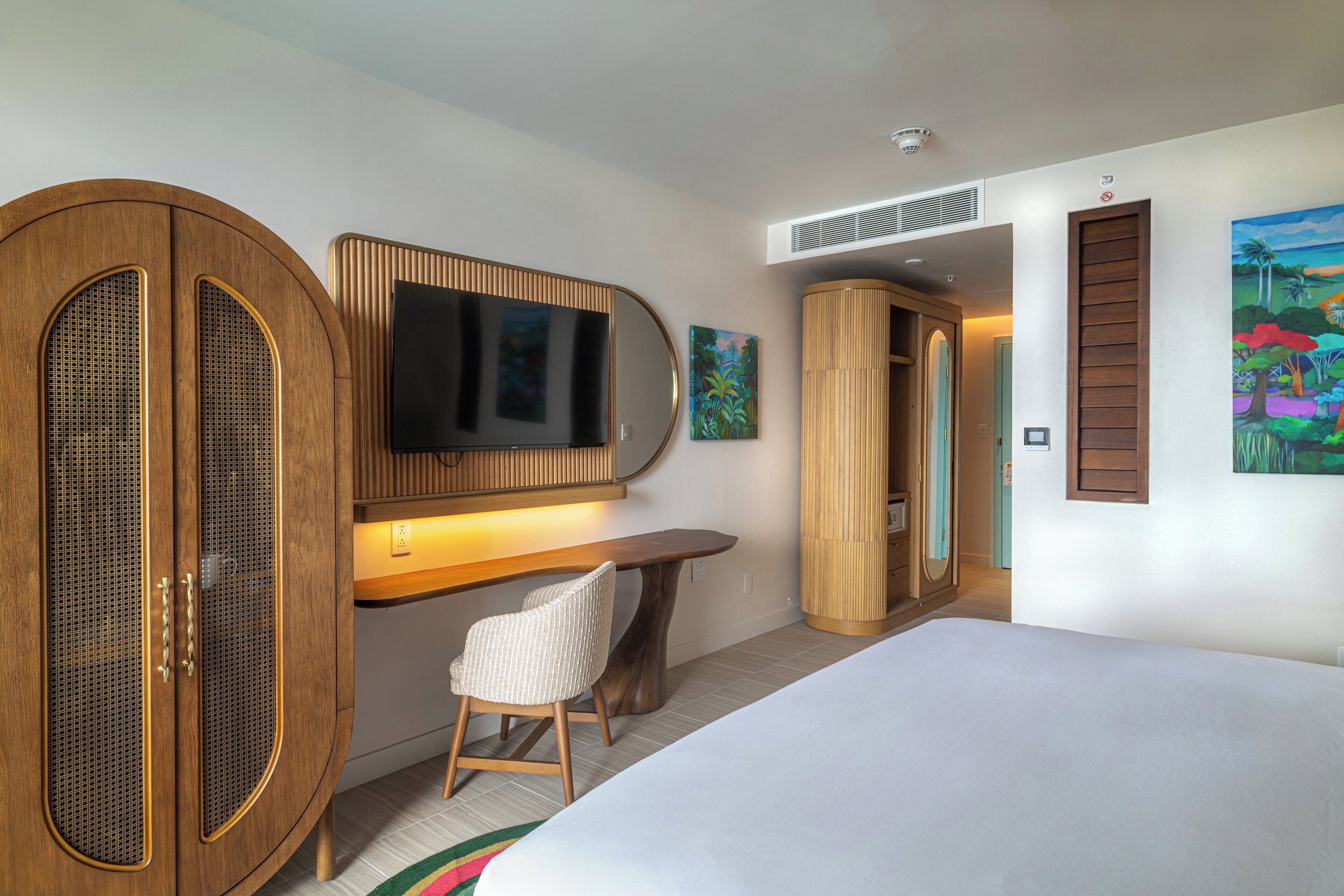 Una habitación de hotel con una cama, un escritorio con una silla, un televisor y un armario.