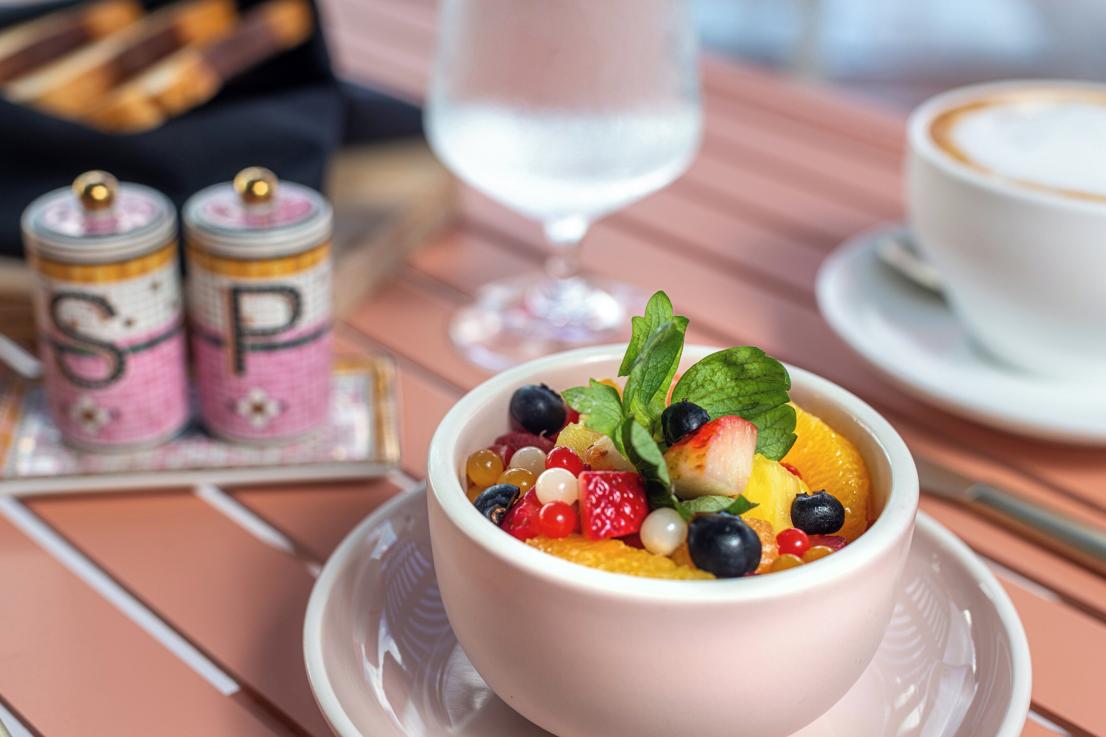 Un tazón de postre con fruta sobre una mesa, un vaso de agua y una taza de café.
