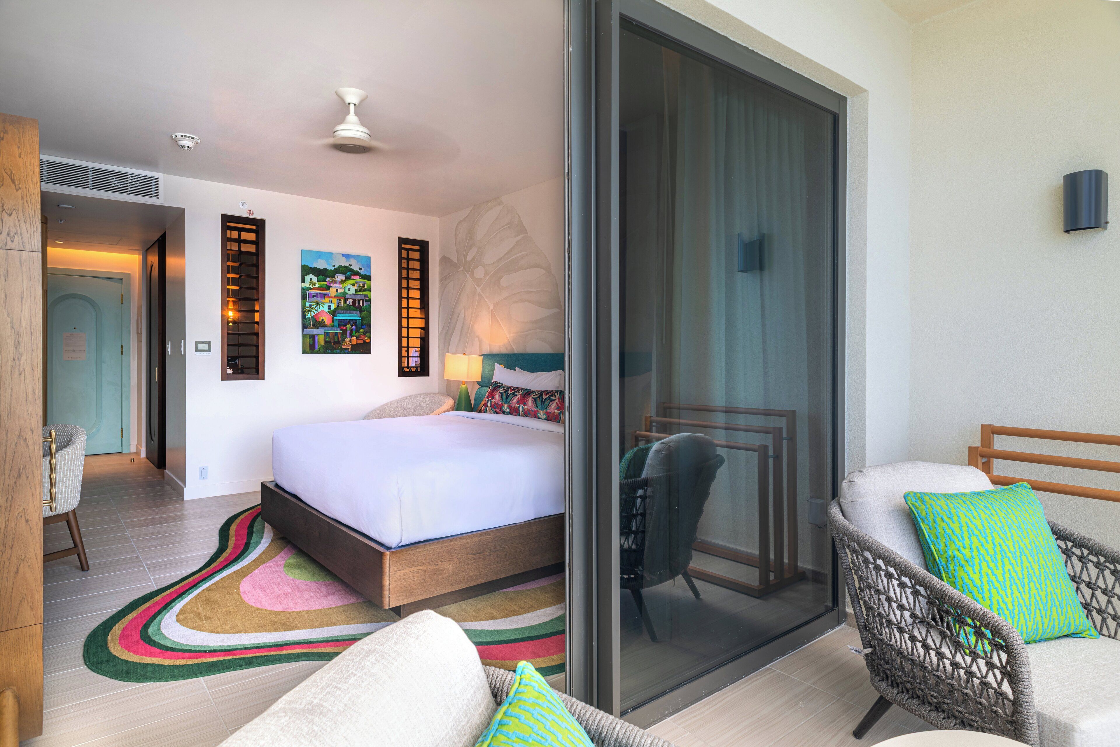 A bedroom with a bed, a chair, a sofa, a large window, and a sliding glass door.