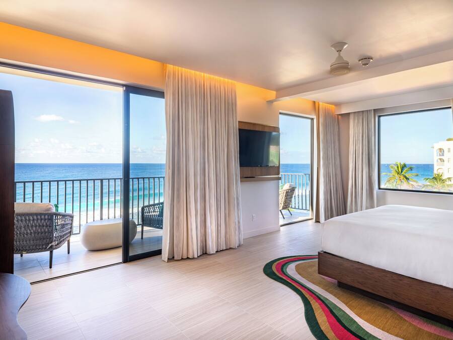 A hotel room with a large bed, a TV, a balcony with a view of the ocean, and a chair.