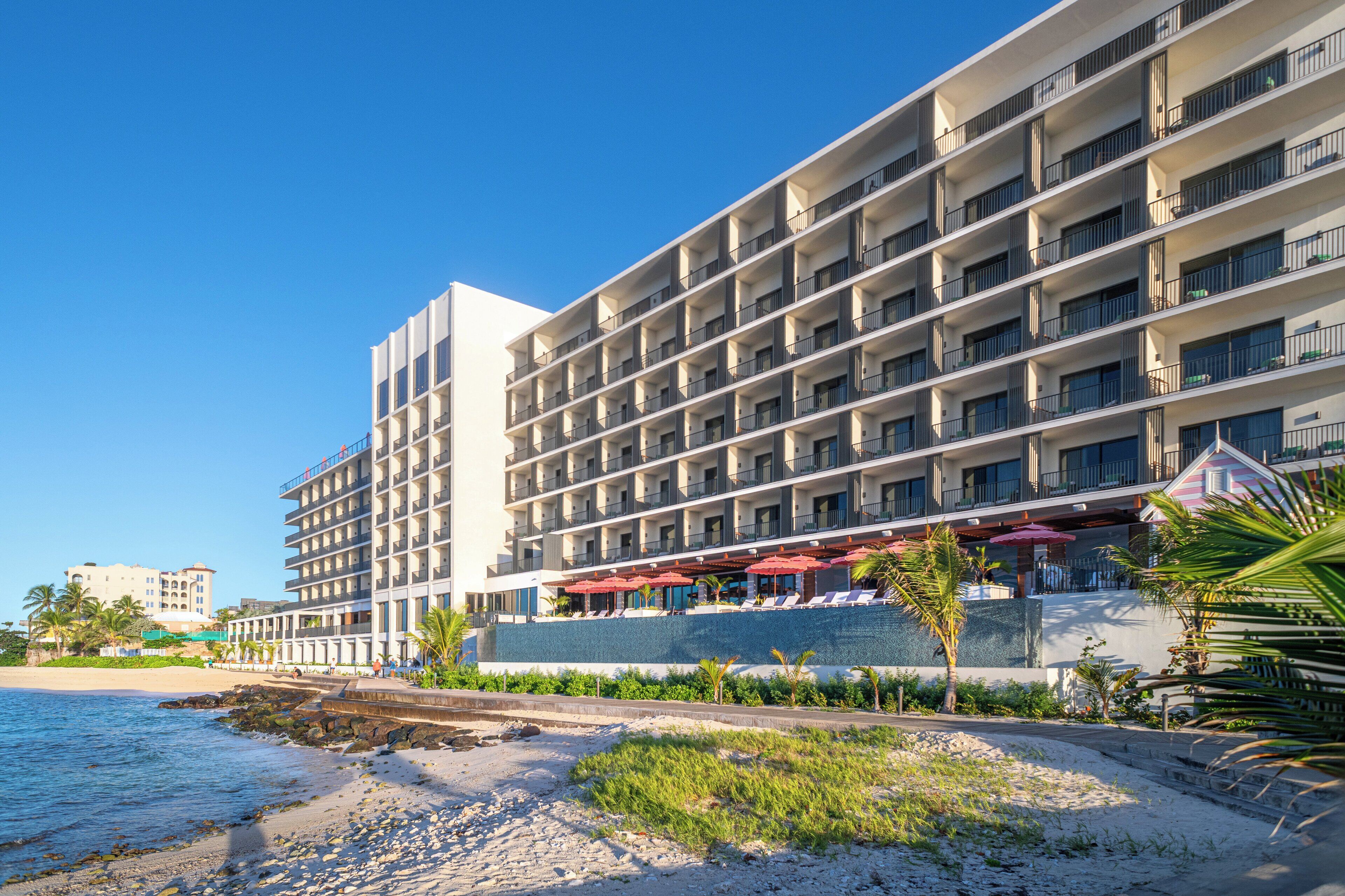 Ein mehrstöckiges Hotel mit Balkonen, einem Poolbereich und Blick auf den Strand.