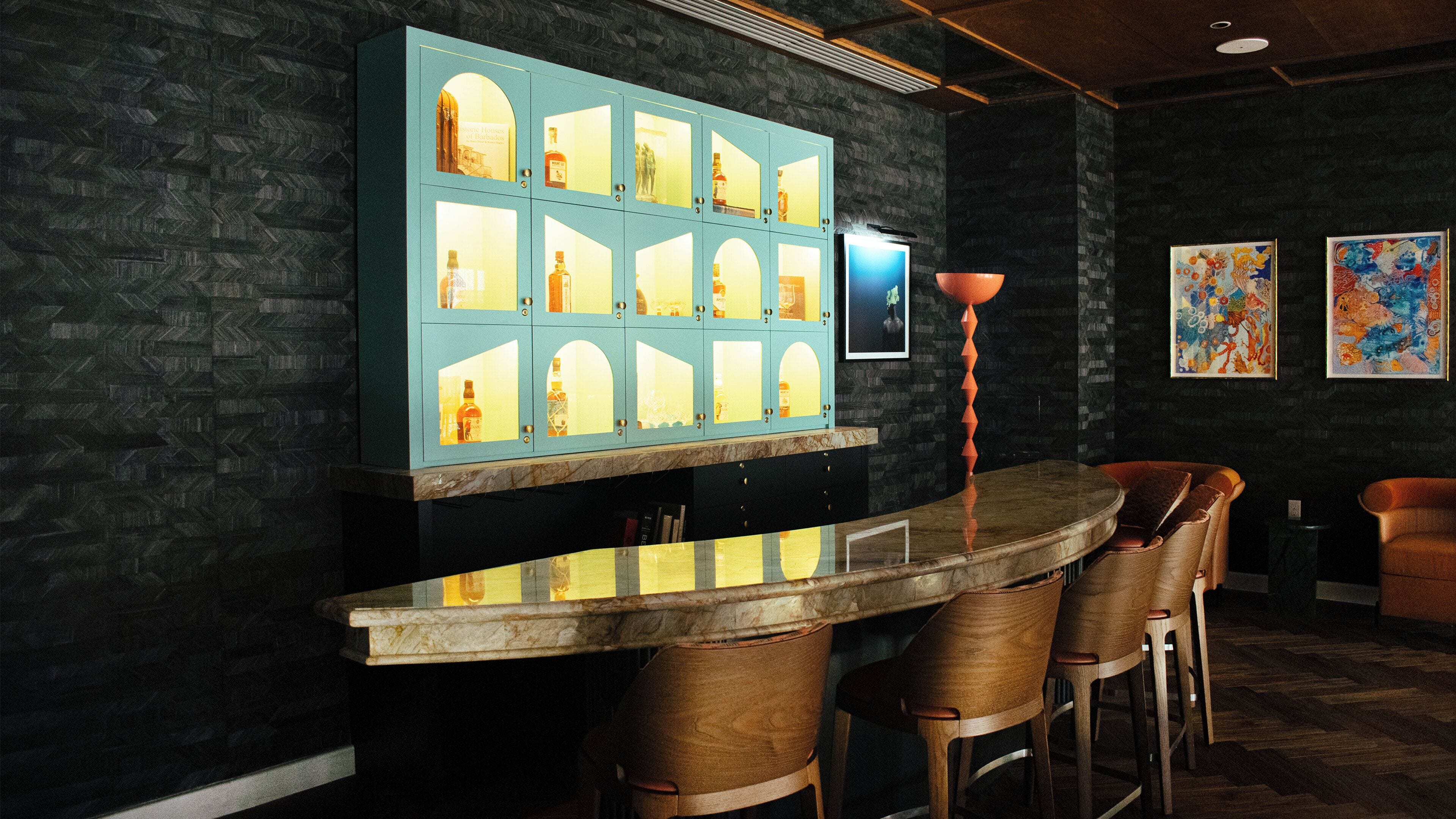 A bar area with a marble countertop, wooden chairs, a teal cabinet with glass doors, and artwork on the walls.
