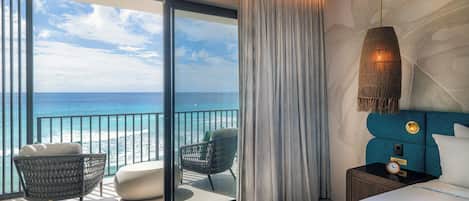 Ein Hotelzimmer mit Balkon und Meerblick, ein Bett mit Kopfteil, ein Nachttisch mit einer Uhr und eine Hängelampe.