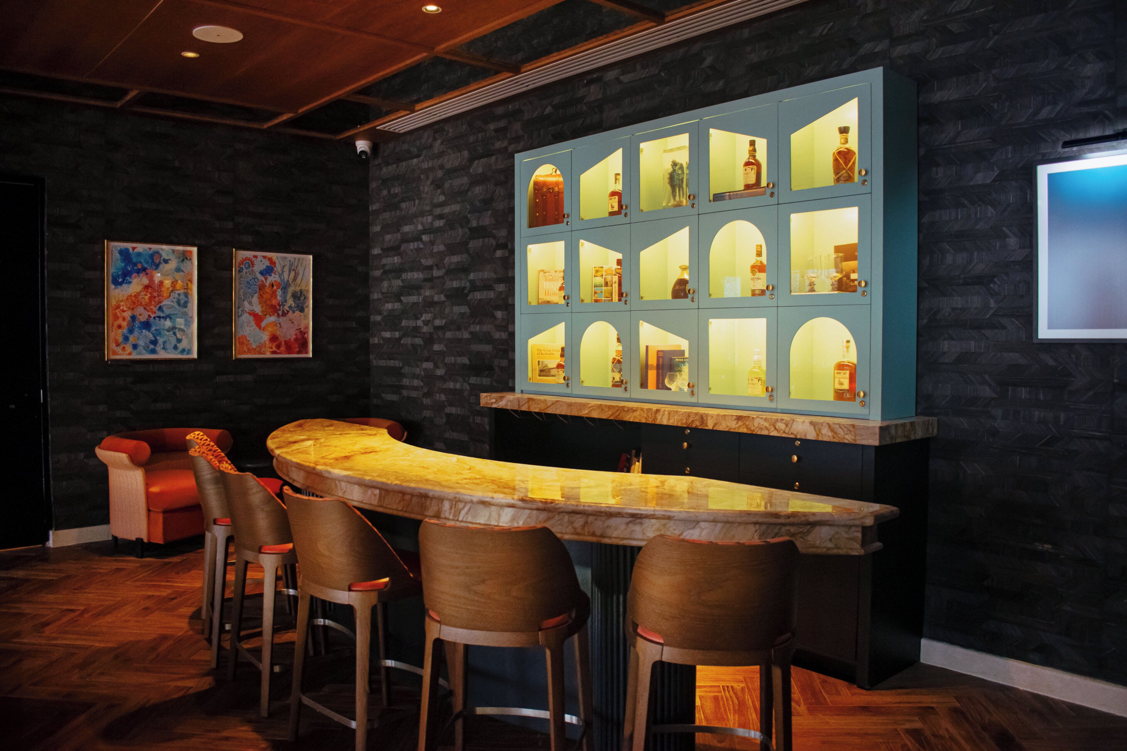 A bar area with a curved counter, wooden stools, and a stone wall backdrop.