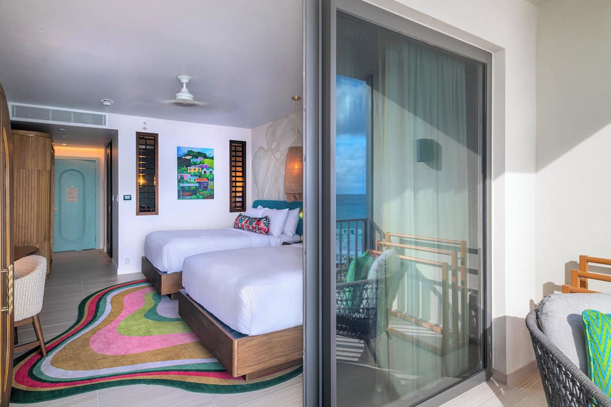 A hotel room with a large bed, a balcony with a view, and a chair by the window.