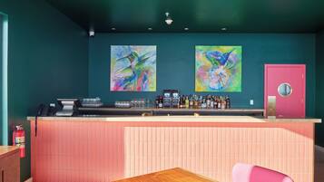 A bar area with a counter, two abstract paintings, a pink door, and a fire extinguisher.