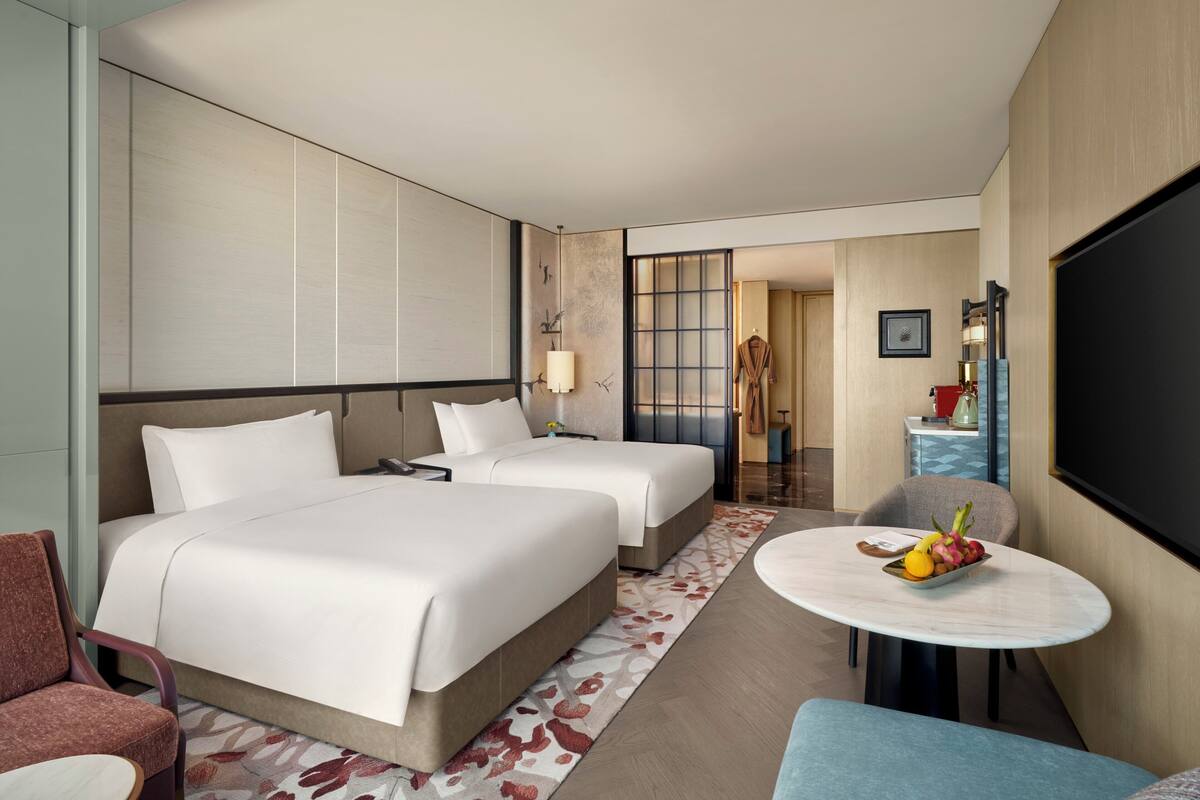 A hotel room with two beds, a sitting area with a table, and a TV.