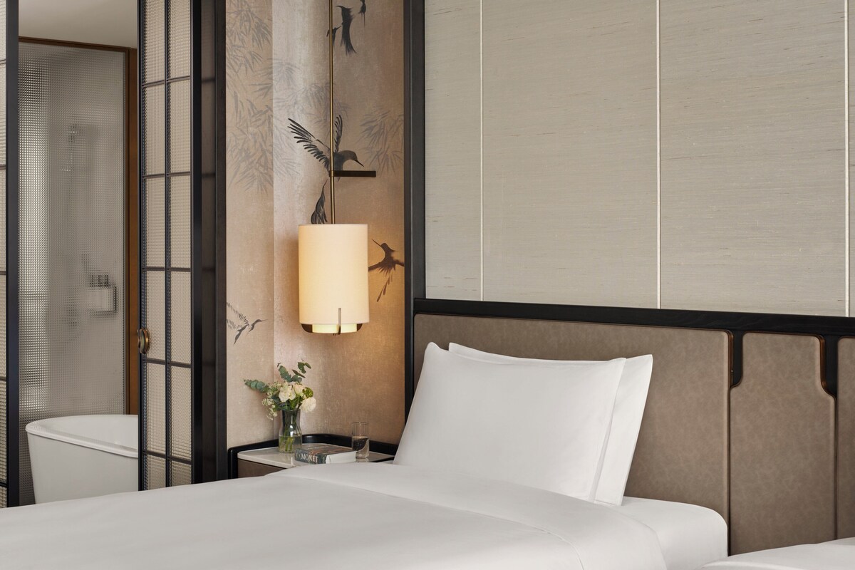 Habitación de hotel con cama, mesita de noche, lámpara y un panel decorativo en la pared.