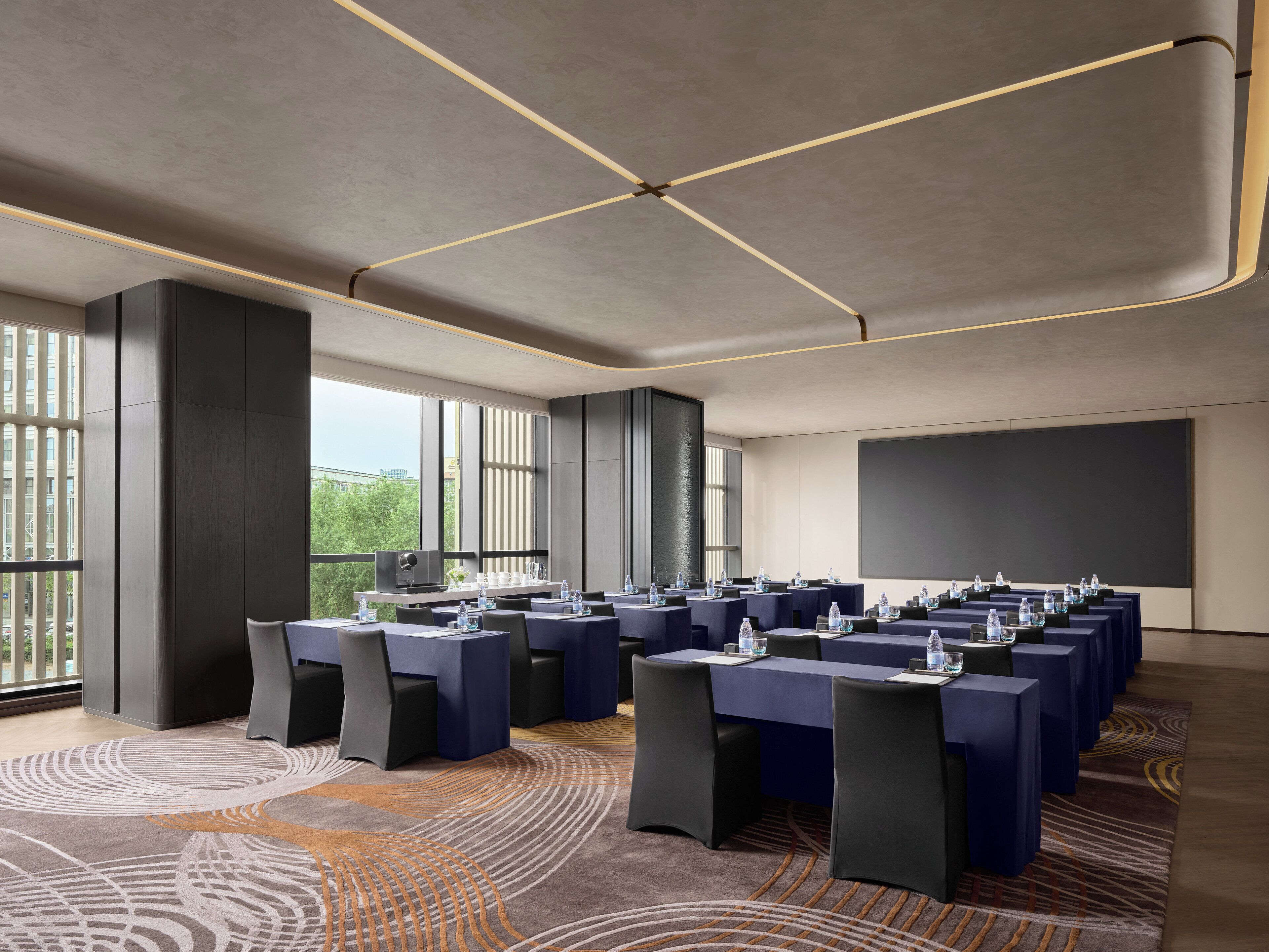A conference room with multiple tables, chairs, and a large screen.