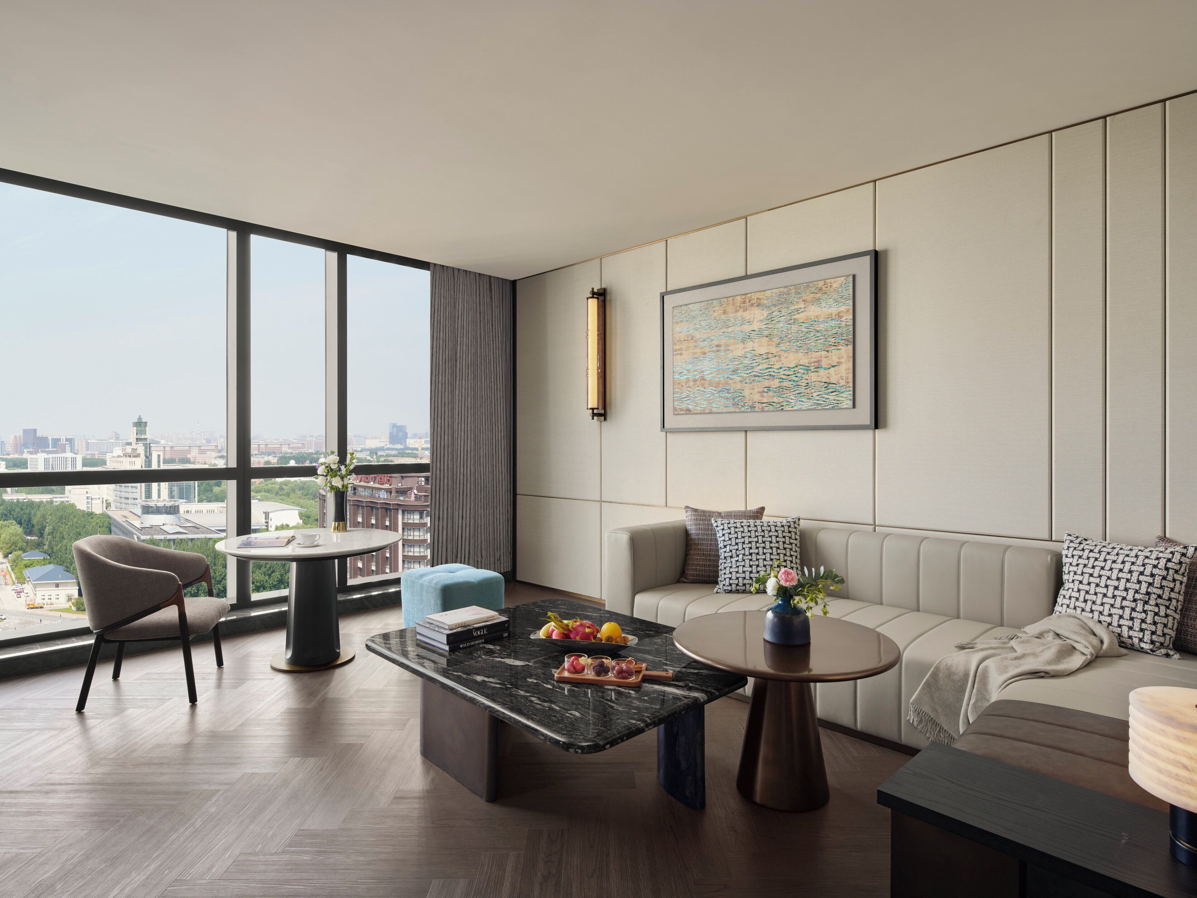 Una sala de estar moderna con un sofá, una mesa de centro y vistas de la ciudad a través de amplios ventanales.