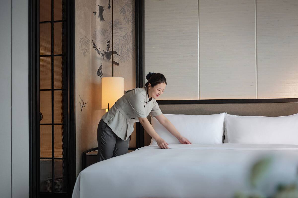A hotel room with a neatly made bed, a wall-mounted lamp, and a decorative panel with birds.