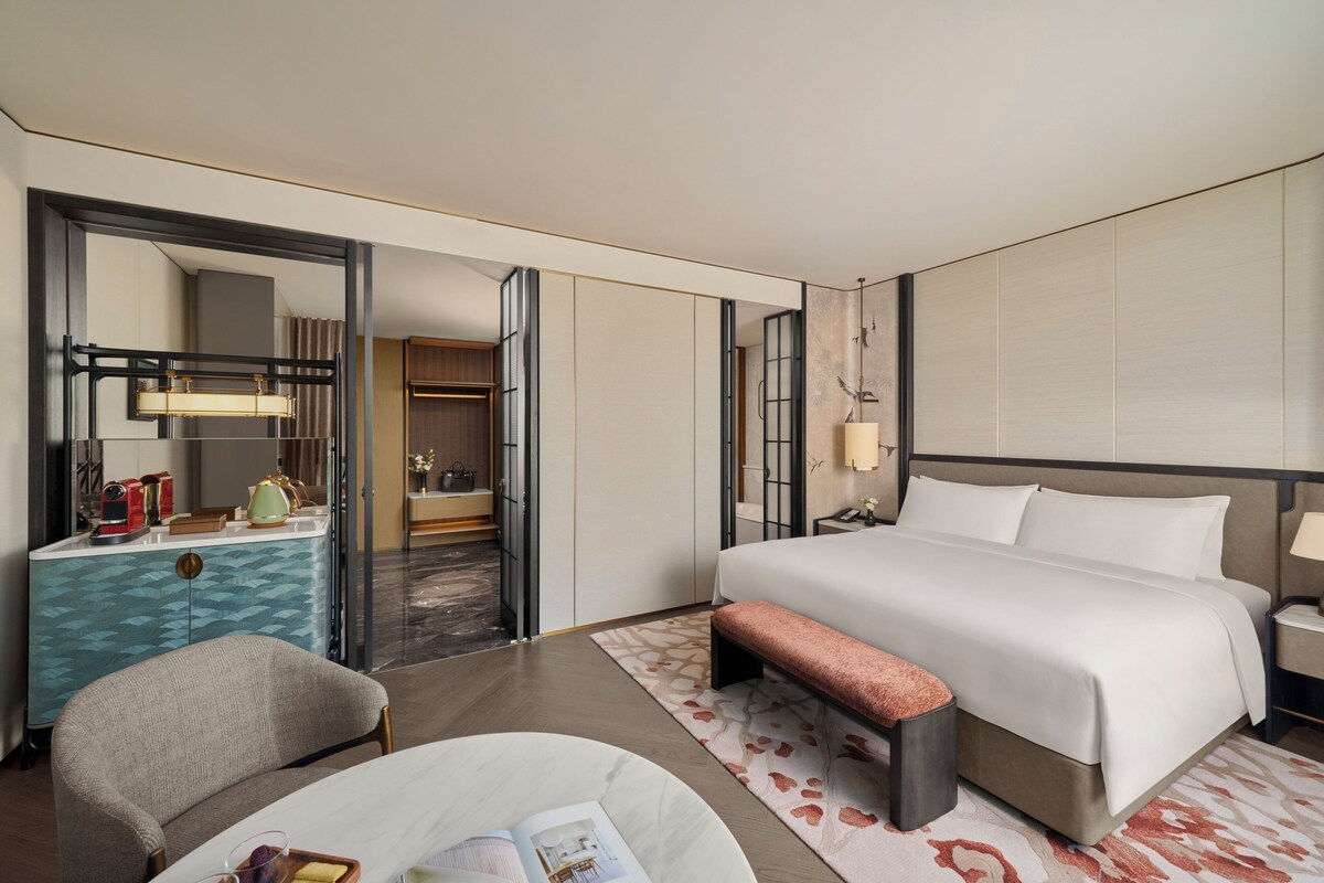 Habitación de hotel con una cama grande, una mesita de noche, una silla, un escritorio con lámpara, un armario y un espejo.