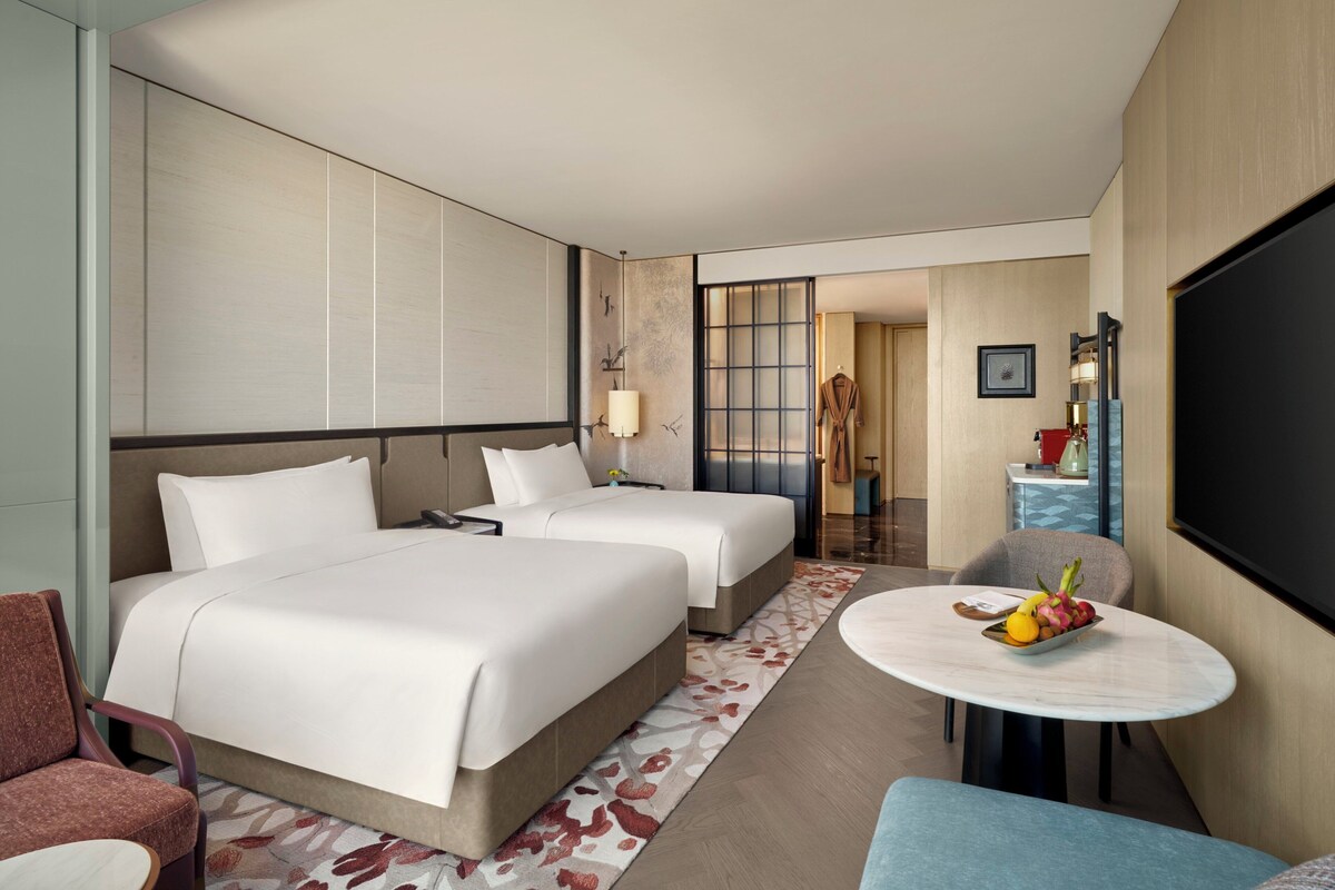 Habitación de hotel con dos camas, una zona de estar con una mesa y un televisor.