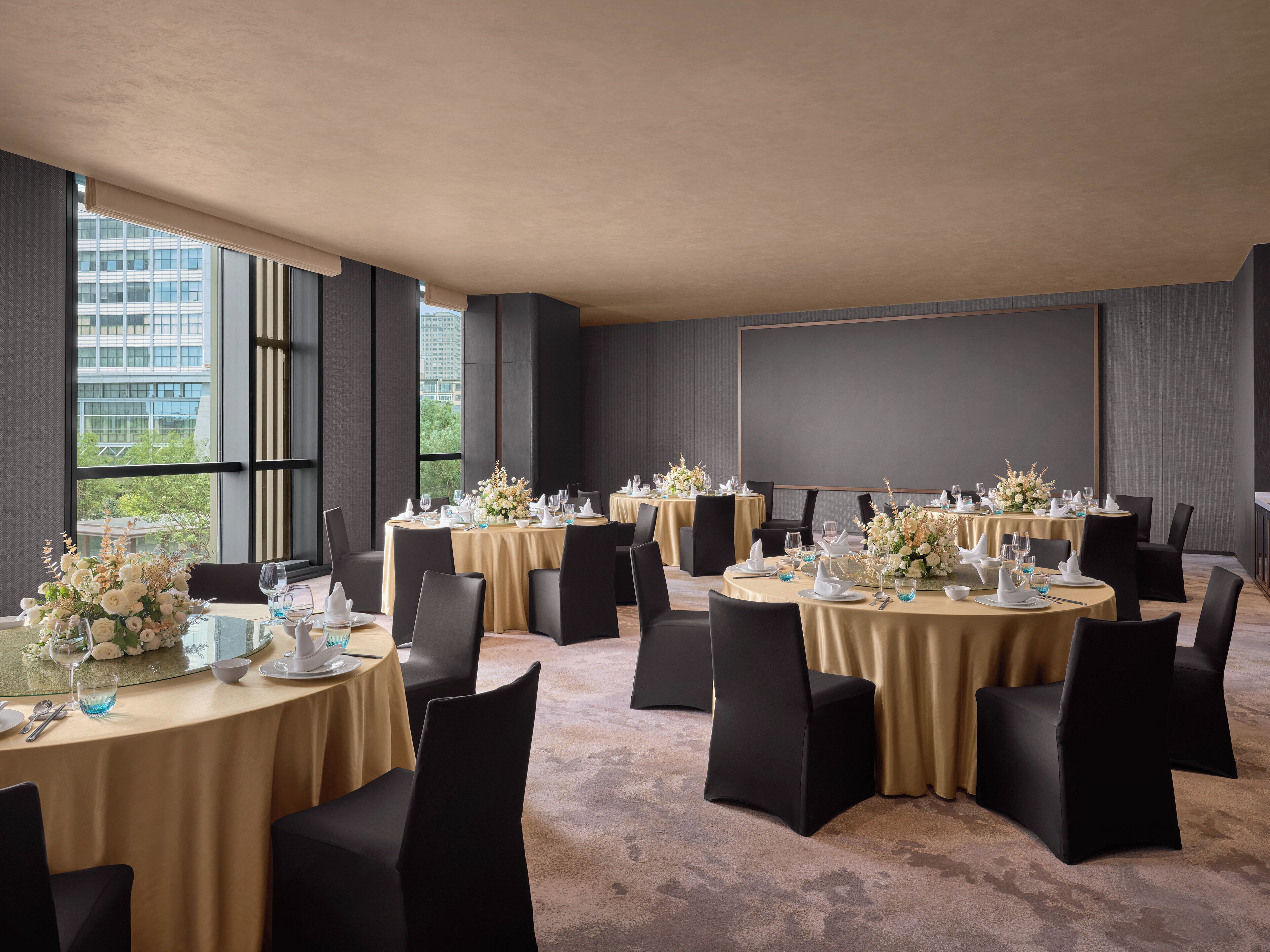 A conference room with multiple tables set for a formal event, featuring black chairs and gold tablecloths.