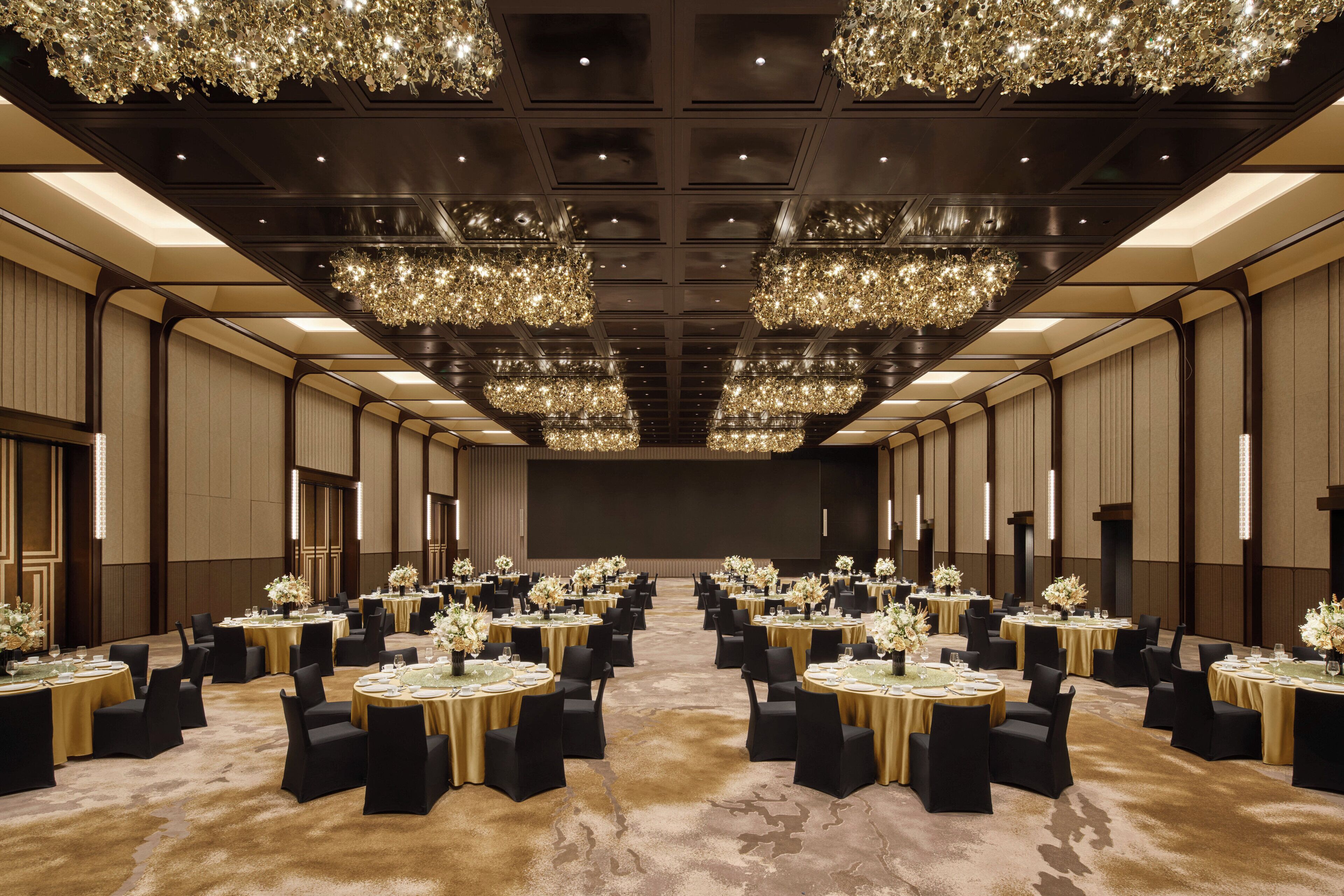 A large, well-lit banquet hall with multiple round tables, each set with black chairs and white tablecloths.