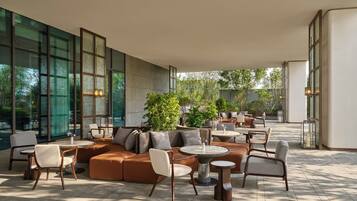 A spacious outdoor lounge area with a mix of seating options including sofas, chairs, and round tables.