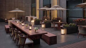 An outdoor dining area with tables, chairs, and umbrellas, surrounded by large windows and potted plants. - Intercontinental Changchun High Tech Zone by IHG (Changchun)