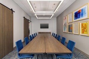 Une salle de conférence avec une longue table, des chaises bleues, un téléviseur à écran plat et des œuvres d’art encadrées accrochées au mur.