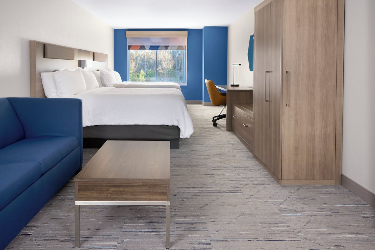 A modern hotel room with a large bed, a blue sofa, a wooden desk, and a wardrobe.