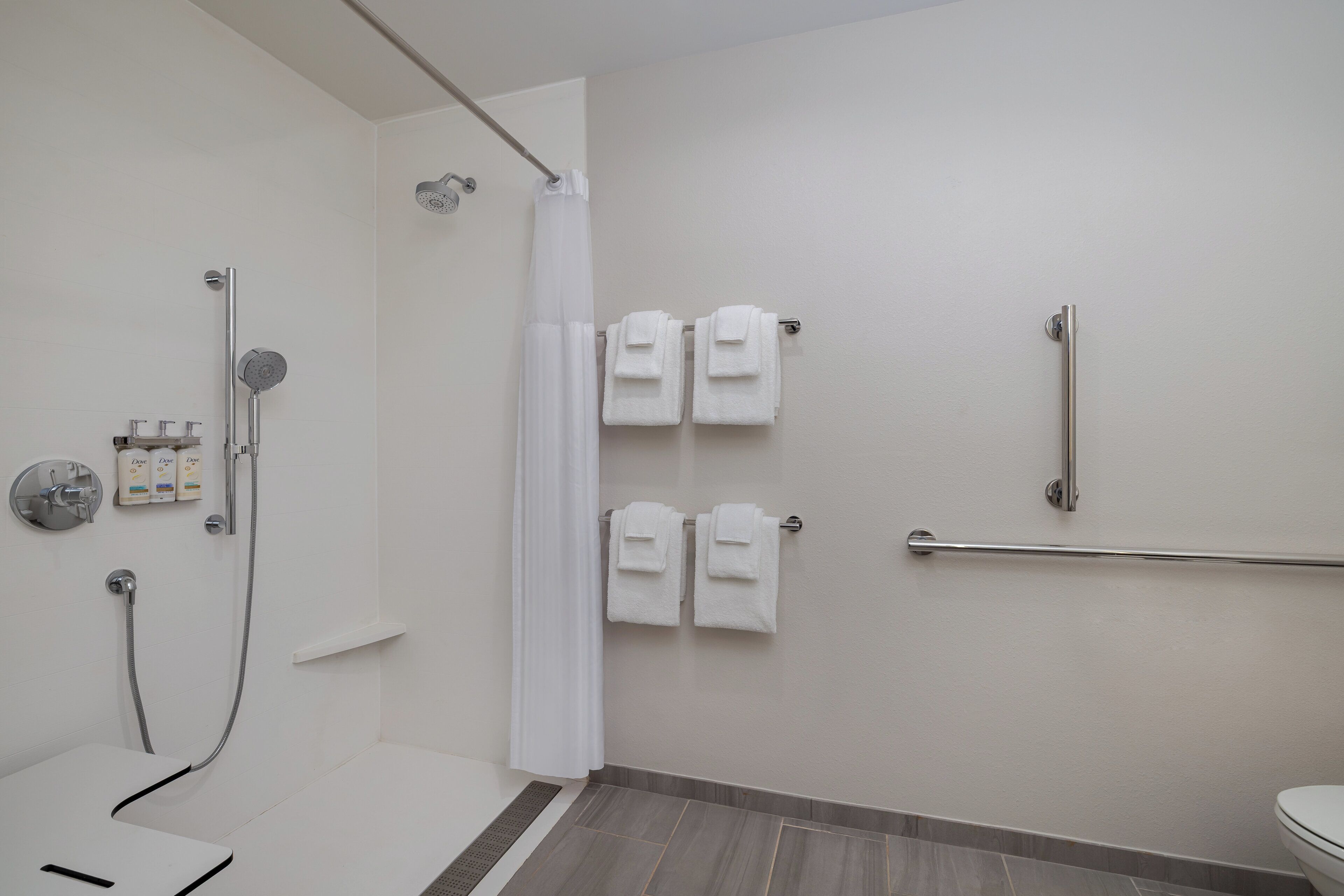 Un baño moderno con ducha, inodoro y barra de apoyo.