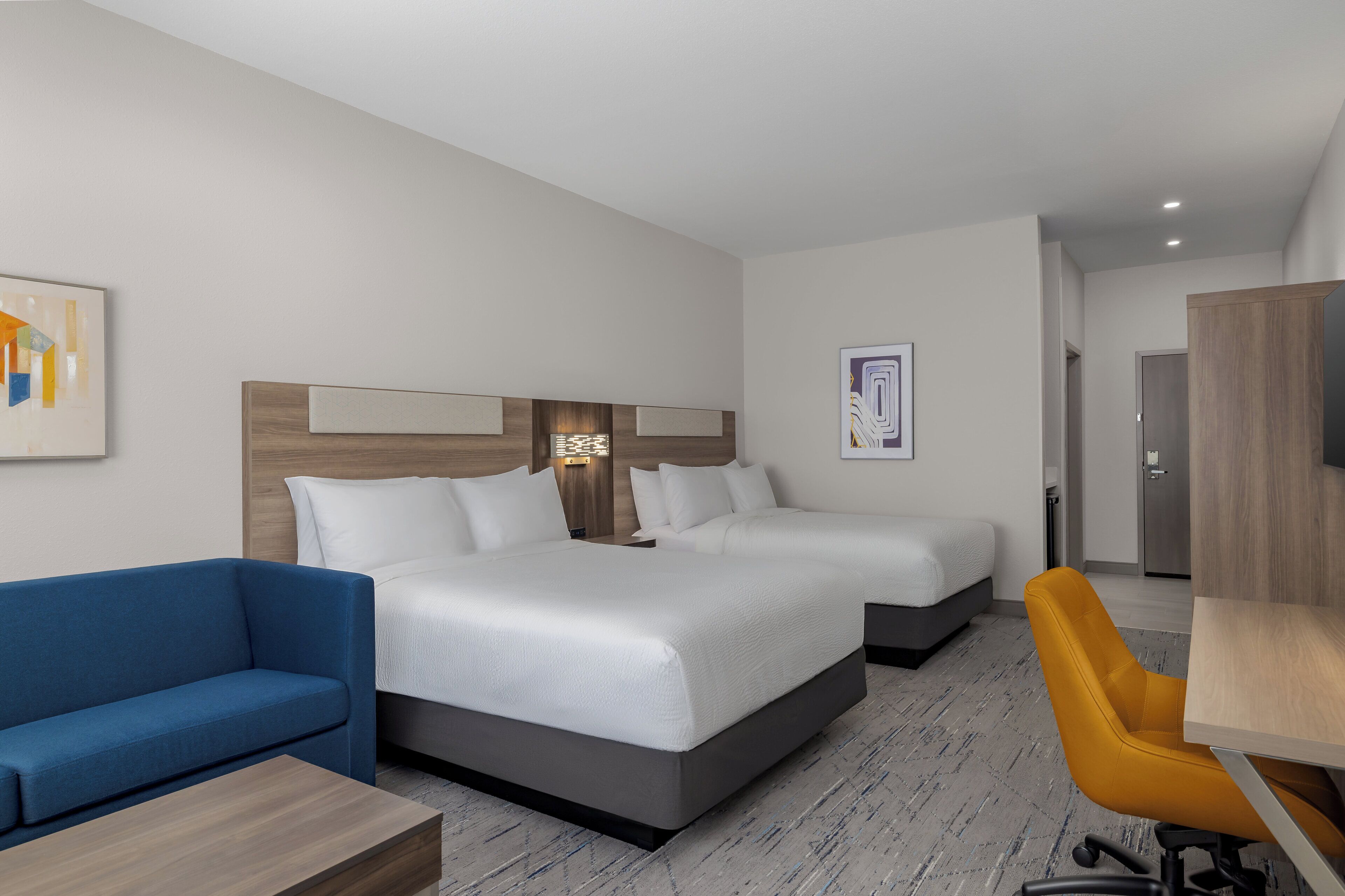 Een hotelkamer met een groot bed, twee nachtkastjes, een blauwe bank, een gele stoel en een houten bureau.