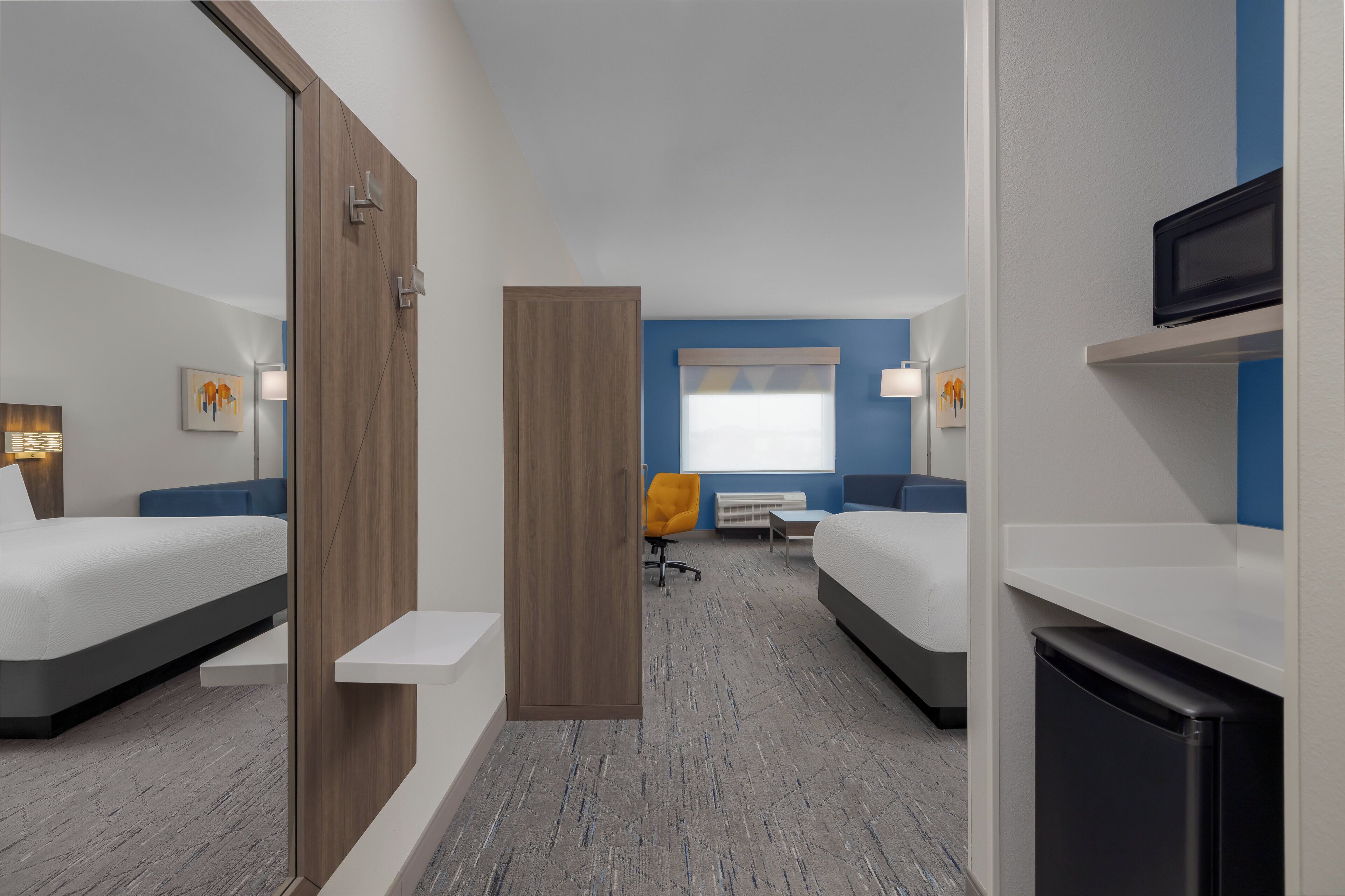A hotel room with two beds, a desk, a chair, a television, and a microwave.