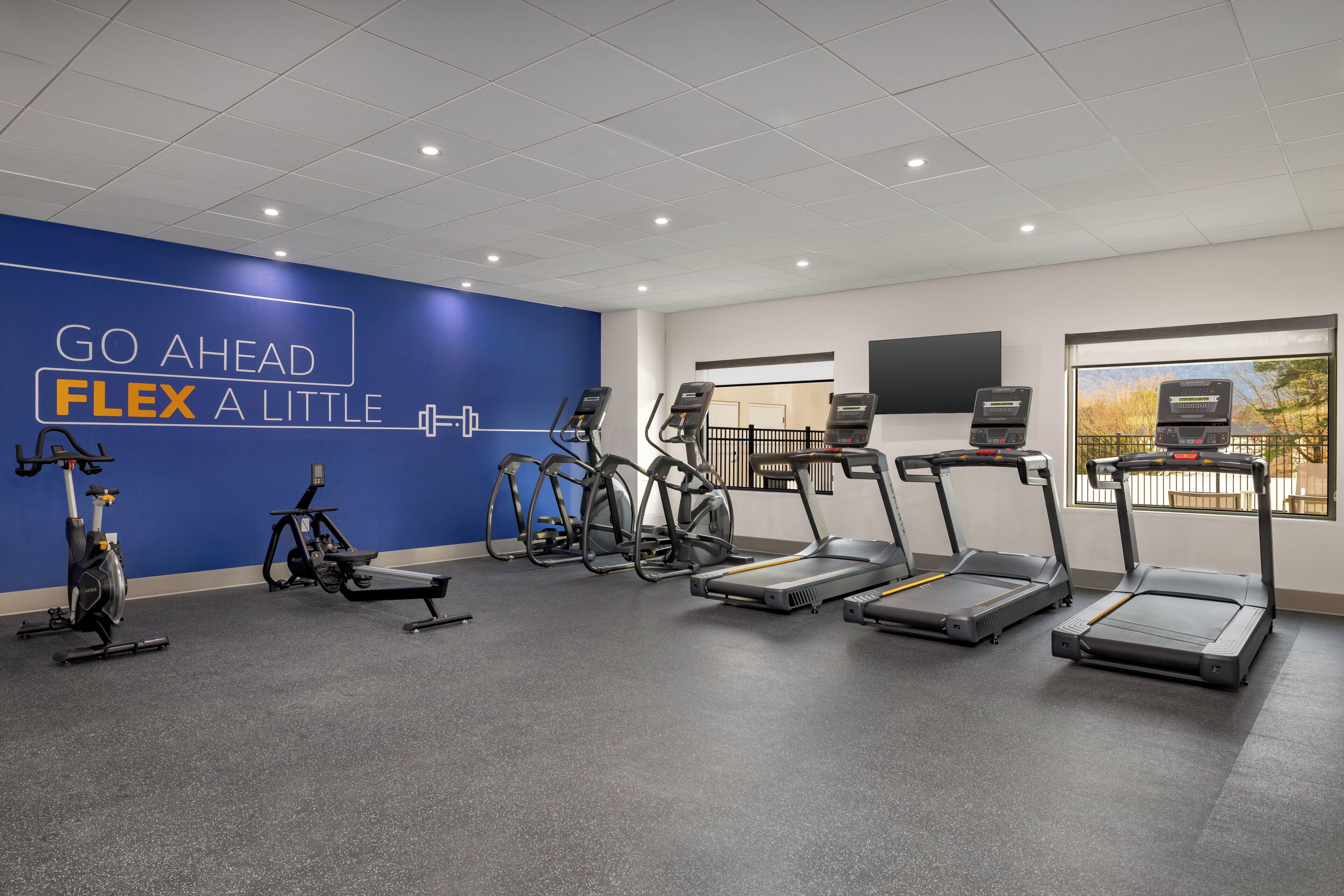 Een sportschool met loopbanden, elliptische trainers en een blauwe muur met motiverende teksten.