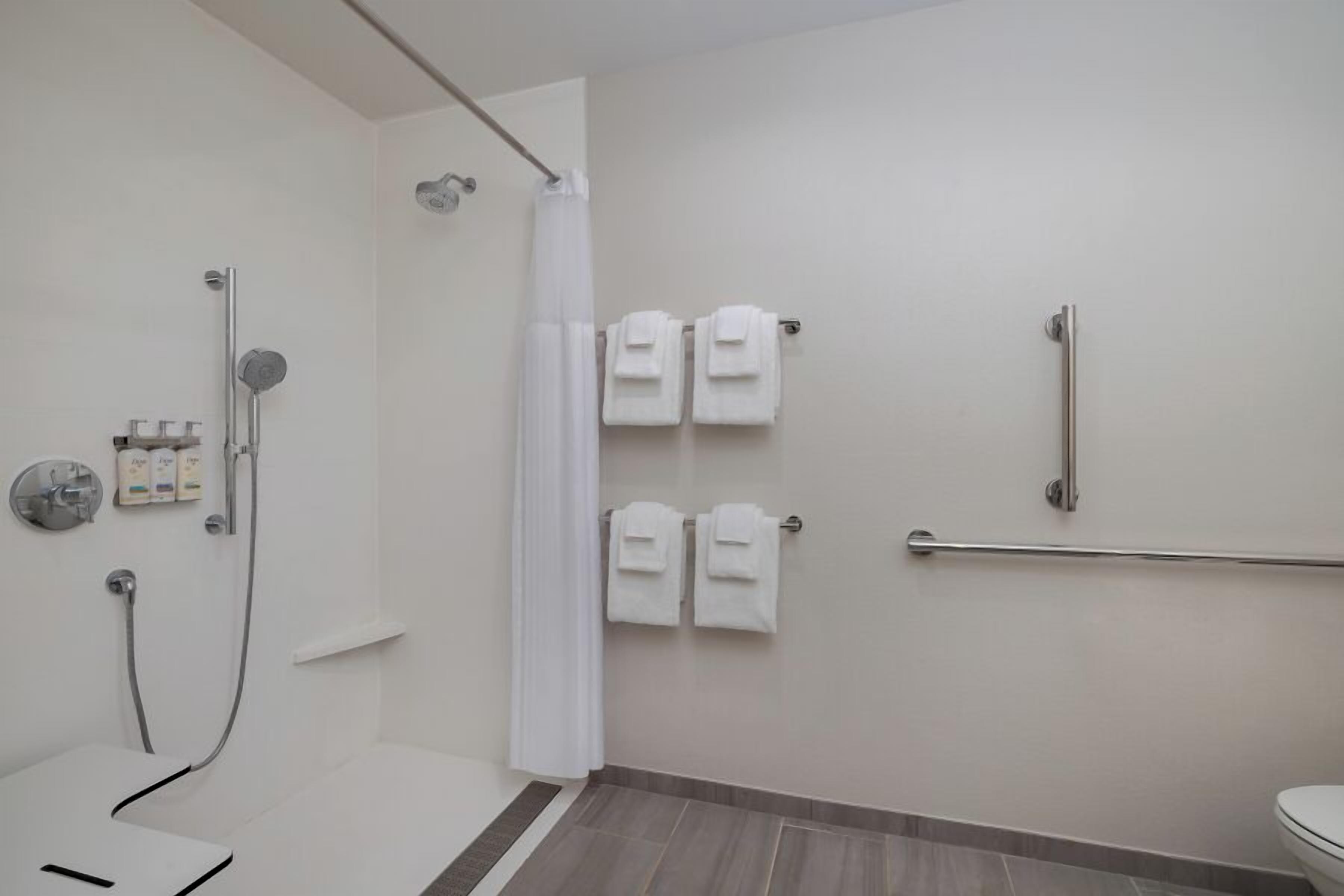 A modern bathroom with a shower, toilet, and handrails.
