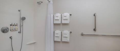 A modern bathroom with a shower, toilet, and handrails.