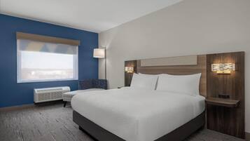 Une chambre d’hôtel avec un grand lit, une fenêtre avec des stores, une table de chevet avec une lampe et un luminaire fixé au mur.