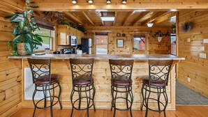 A wooden cabin interior with a kitchen area, bar stools, and a large window. - Cozy Cottage w/ Views, Hot Tub & Games (Sevierville)