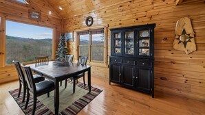 A wooden cabin interior with a dining table, chairs, a Christmas tree, and a cabinet with glass doors. - Cozy Cottage w/ Views, Hot Tub & Games (Sevierville)