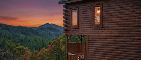 A log cabin with a balcony overlooking a forested valley.