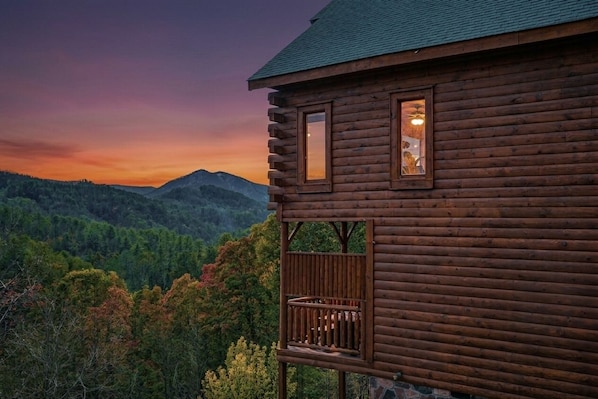 A log cabin with a balcony overlooking a forested valley.