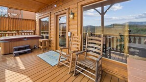 A wooden deck with a hot tub, wooden chairs, and a view of the mountains. - Cozy Cottage w/ Views, Hot Tub & Games (Sevierville)