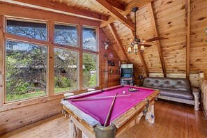 A wooden interior with a pool table, a leather sofa, and a ceiling fan.