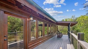 Eine Holzterrasse mit großen Fenstern, einer Pergola und Sitzgelegenheiten im Freien.