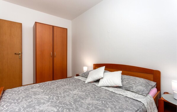 Un dormitorio con una cama, dos armarios de madera, una mesita de noche con una lámpara y una mesita auxiliar.