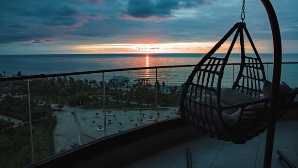 Un balcone con una poltrona amaca che si affaccia su un tramonto sul mare.